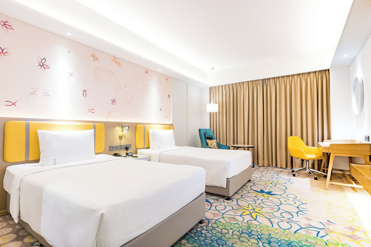 Een hotelkamer met twee bedden, een bureau, een stoel en een kamerbreed tapijt met patroon.