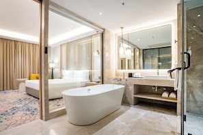 Une salle de bain d’hôtel moderne avec une baignoire sur pieds, un grand miroir et un espace douche séparé.