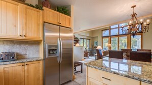 A kitchen with wooden cabinets, a stainless steel refrigerator, granite countertops, and a chandelier. - The Mountain Retreat 3 Bedroom Townhouse by Alpine Lodging Telluride (Telluride)