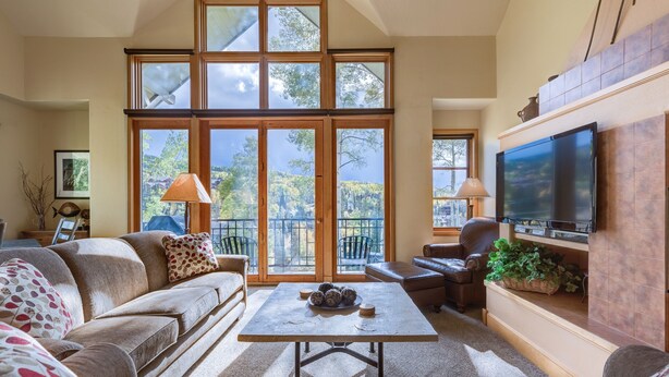 A spacious living room with a large window, a flat-screen TV, and a comfortable seating area. - The Mountain Retreat 3 Bedroom Townhouse by Alpine Lodging Telluride (Telluride)