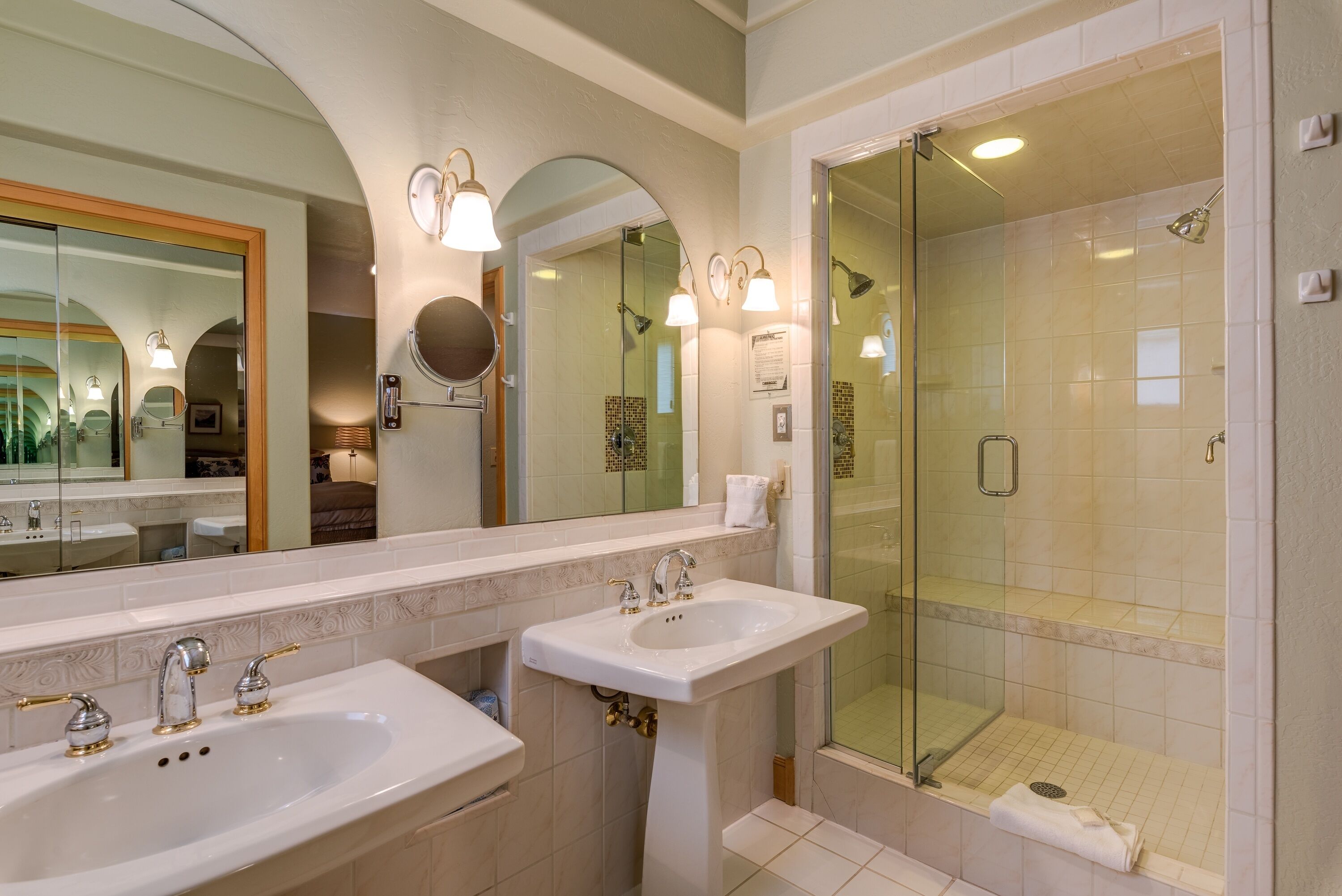 A bathroom with two sinks, a large mirror, and a glass-enclosed shower.