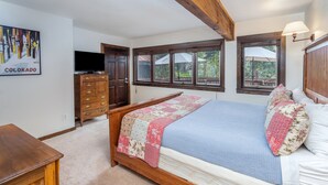 A bedroom with a bed, wooden dresser, television, and windows. - Manitou Lodge 4 Hotel Room by Alpine Lodging Telluride (Telluride)