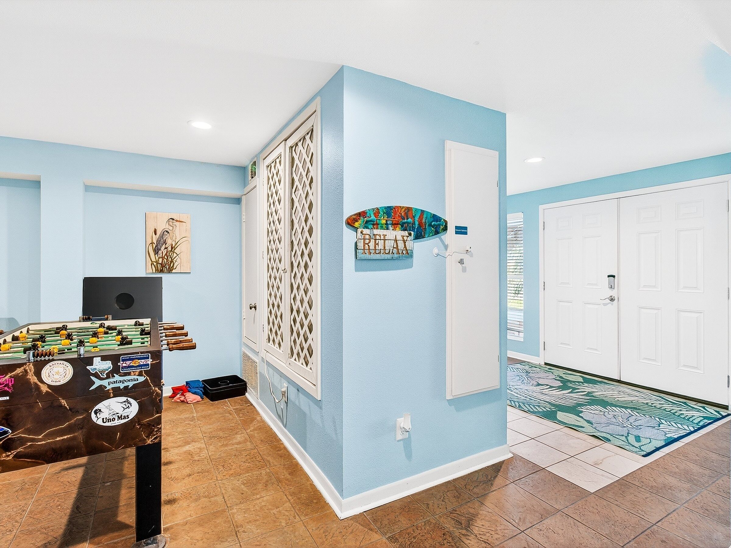 A room with a foosball table, a door with a 'Relax' sign, and a patterned rug.