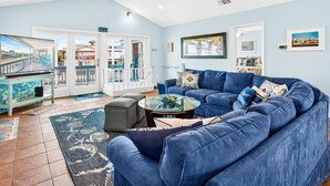 A living room with a blue sofa, a coffee table, and a TV. There are doors leading to an outdoor area with a balcony.