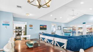 A spacious living area with a dining table, blue sofa, and a kitchen in the background.