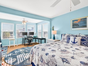 Quarto com cama, escrivaninha, cadeira, computador, abajur e um quadro na parede.