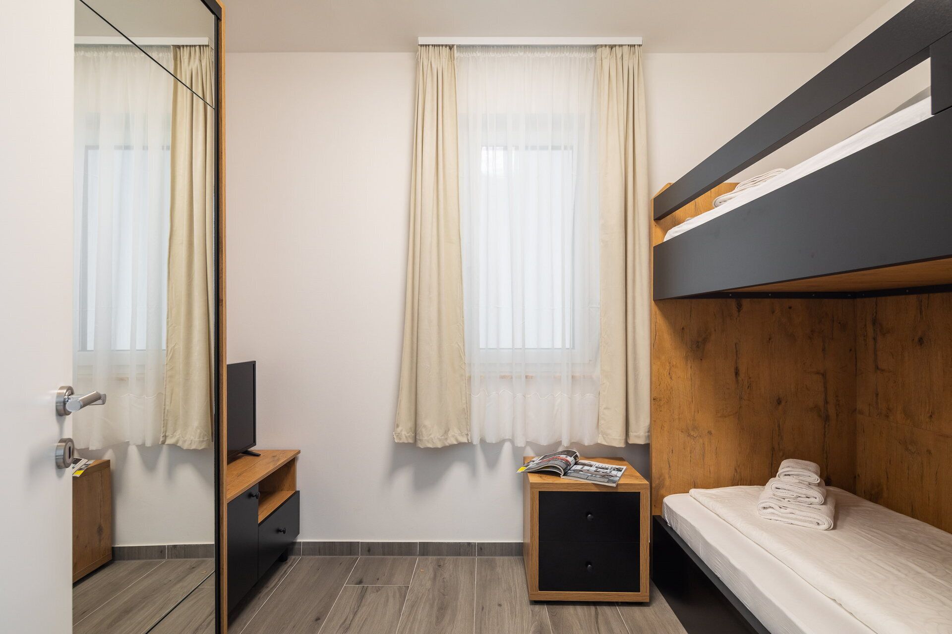 A bedroom with a bunk bed, a wooden nightstand, a small table with a magazine, and a mirror.