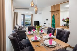 A modern dining area with a wooden table set for six, surrounded by dark upholstered chairs. A television is mounted on the wall, and a large window offers a view of the sea. - Beach Villa Valentina Apartment XI (Okrug Gornji)
