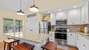 Una cocina con armarios blancos, una isla de granito, electrodomésticos de acero inoxidable e iluminación colgante.