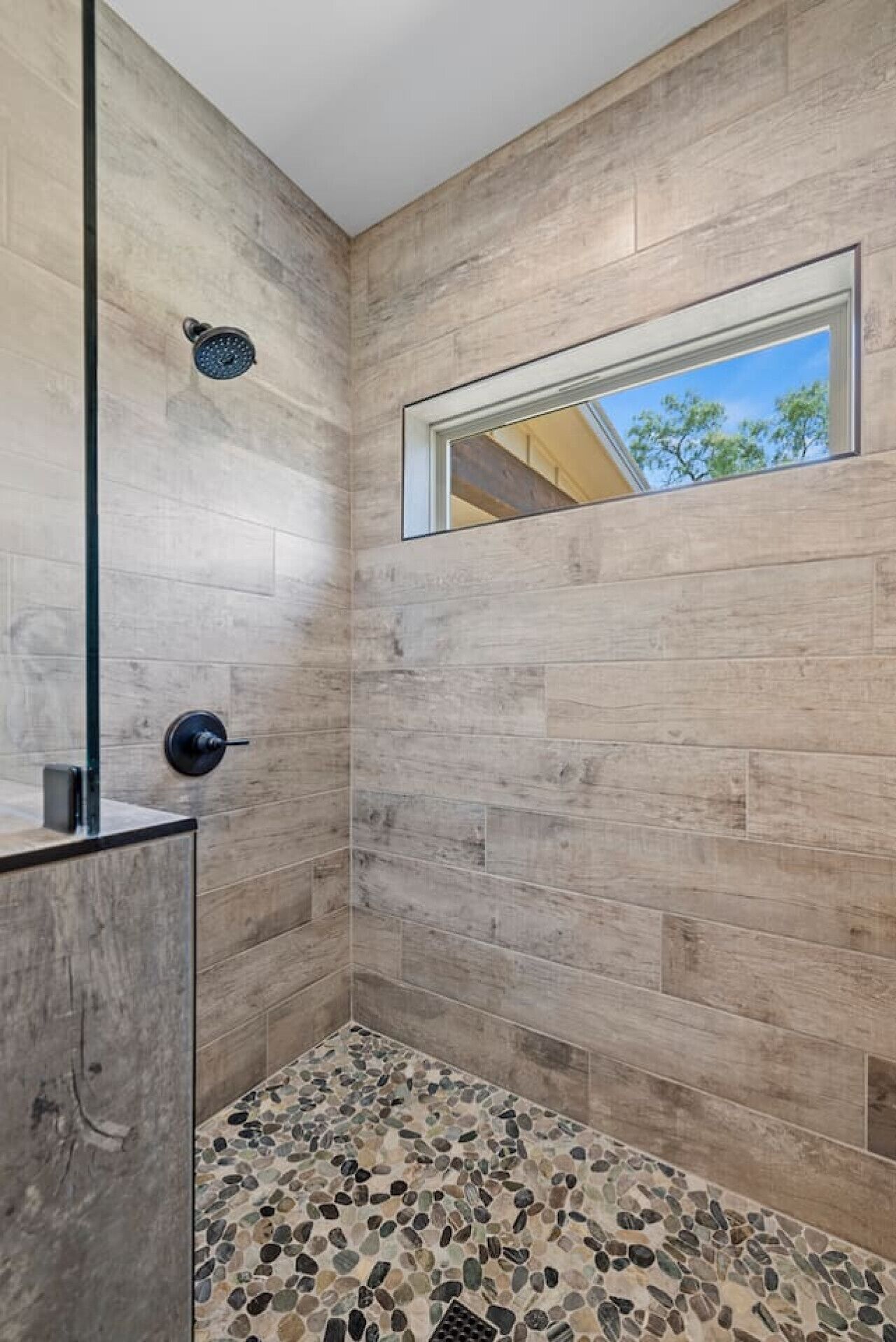 Une douche moderne dotée d’une porte en verre, d’une fenêtre intégrée et d’un sol orné d’un motif de galets.