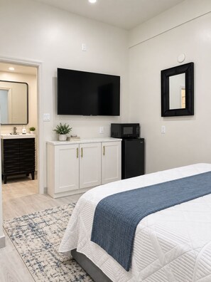 A bedroom with a bed, a flat-screen TV, a microwave, and a dresser.