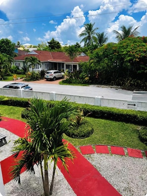 A residential area with a house, parked cars, a red carpet pathway, and a palm tree.