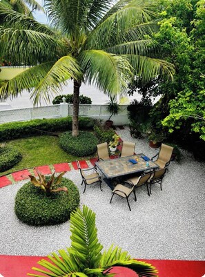 Un patio exterior con una mesa y sillas, rodeado de vegetación exuberante y una palmera.