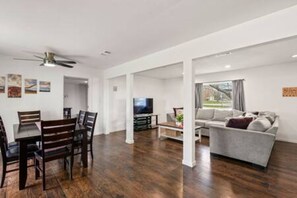 A modern living room with a dining area, a flat-screen TV, and a grey sofa. - FW Monthly + WiFi + Desk + Pet Backyard (Fort Worth)
