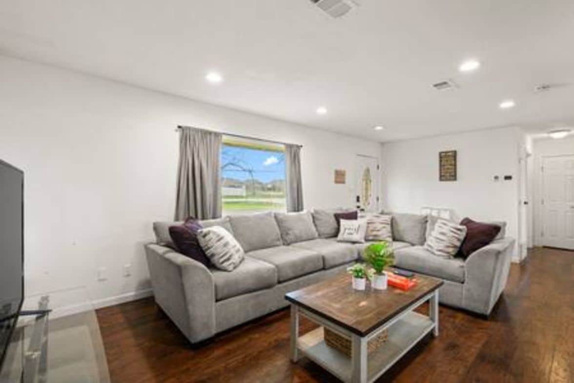 A modern living room with a grey sectional sofa, a wooden coffee table, and a large window with curtains.