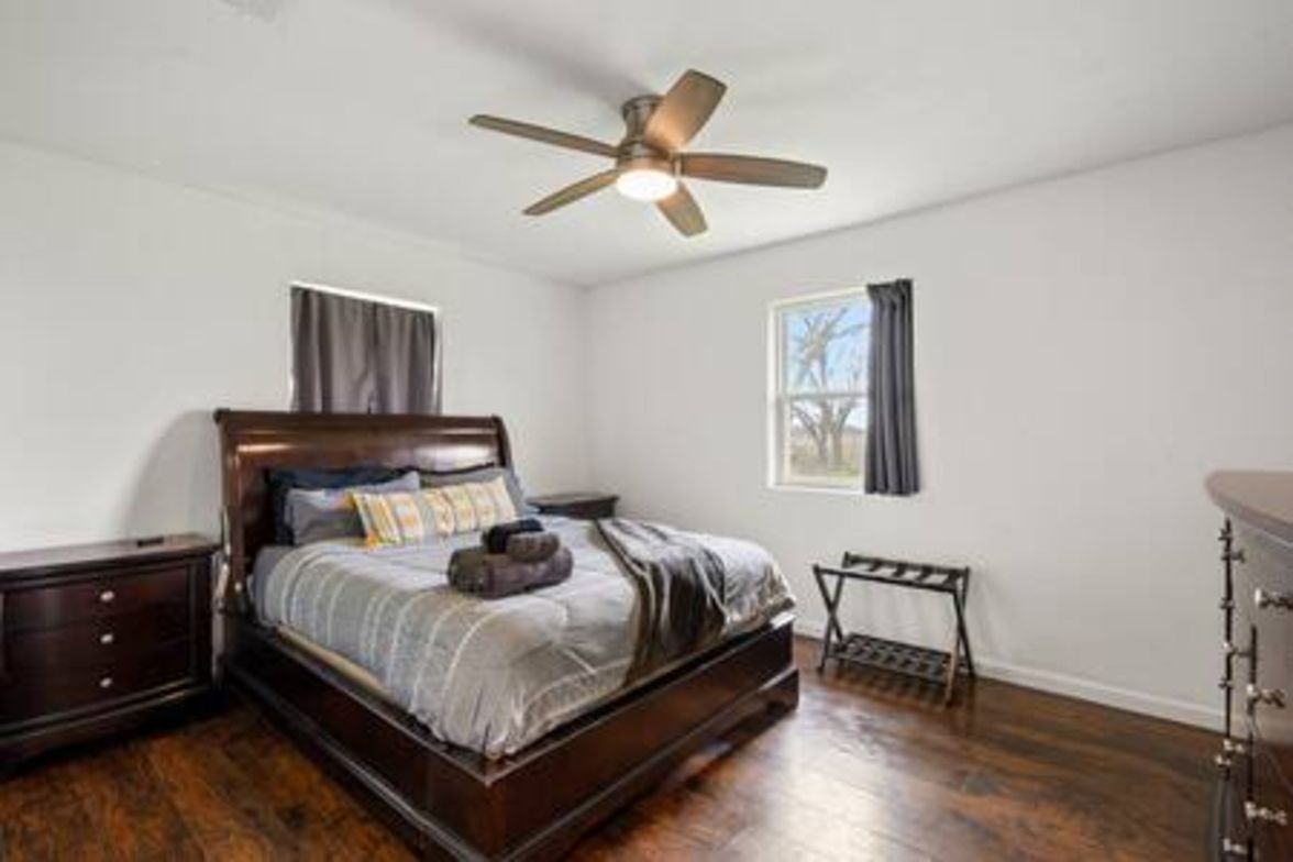 A bedroom with a bed, a nightstand, a dresser, a ceiling fan, and a window with curtains.