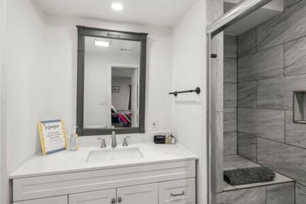 A modern bathroom with a white vanity, a large mirror, and a shower area with grey tiles.
