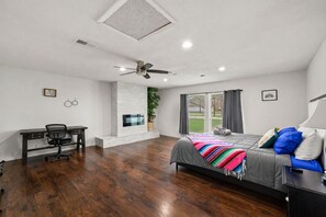 A modern bedroom with a bed, desk, and chair, a ceiling fan, and a view of the outdoors. - Monthly Stays Desk, WIFi, Texas Speedway, Pet Friendly Large Fenced Back (Fort Worth)