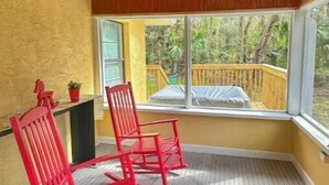A room with a wooden ceiling, a ceiling fan, a window with a view of a wooden deck, and two red rocking chairs. - LemonTree Cottage firepit and hottub, 8 minutes from the beach (New Smyrna Beach)