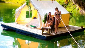A tented structure on a floating platform in a body of water, surrounded by greenery. - Finca Paraiso Glamping (Guatapé)