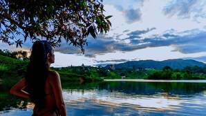 A woman in a bikini standing by a calm lake with a mountain in the background. - Finca Paraiso Glamping (Guatapé)