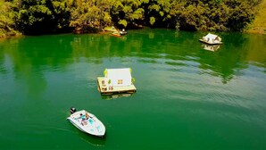 A houseboat on a green river with a dock and a small boat nearby. - Finca Paraiso Glamping (Guatapé)