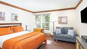 A bedroom with a large bed, a sofa, a TV, and artwork on the walls. - Mountainside Inn 118 1 Bedroom Hotel Room by Alpine Lodging Telluride (Telluride)