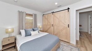 Ein Schlafzimmer mit einem Bett, Nachttischen, einem Holzschrank und einem Fenster mit Vorhängen.