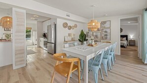 Eine moderne Küche mit Edelstahlgeräten, ein Essbereich mit einem weißen Tisch und blauen Stühlen sowie ein Schlafzimmer mit Bett und Nachttisch.