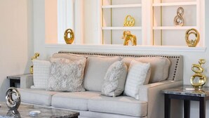 A living room with a beige sofa, a marble coffee table, and a white wall with shelves containing decorative items. - Elegant and cozy 3 bedroom/2 full bath new home (San Antonio)