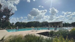 Une piscine avec des chaises longues, un espace de détente couvert et un bâtiment en arrière-plan.