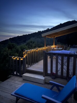 En träaltan med en pergola, ljusslingor och ett bord med stolar.