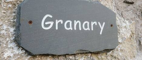 A slate sign with the word "Granary" on a stone wall.