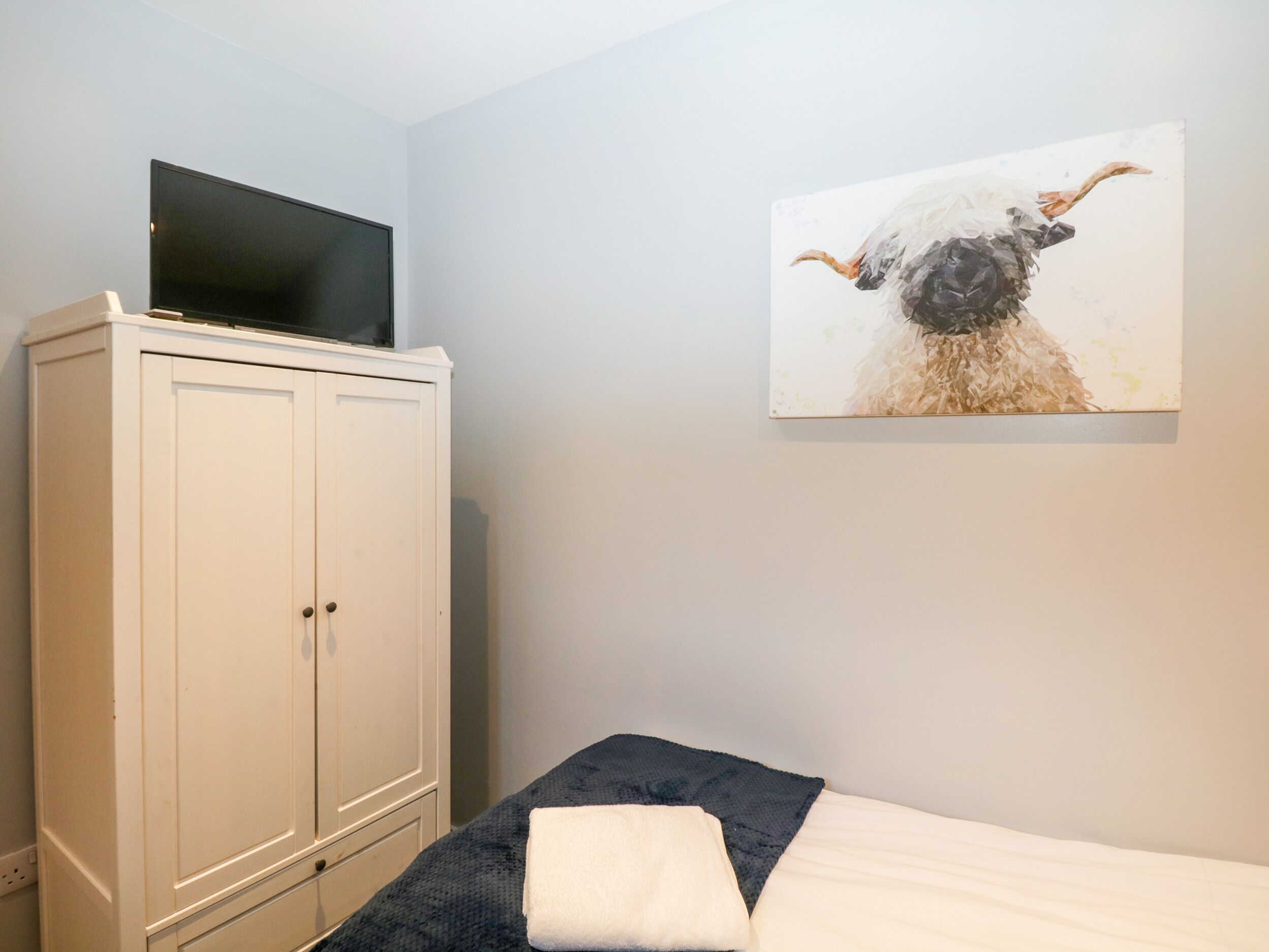 A bedroom with a bed, a TV on a cabinet, and a painting on the wall.