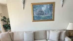 En beige hörnsoffa med ett tillhörande fotstöd, en inramad landskapsmålning och väggmonterade vägglampor.