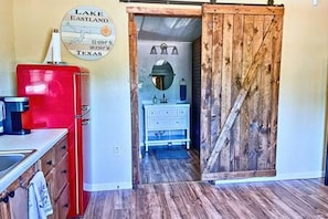 A kitchen with a red refrigerator, a white cabinet, and a wooden door leading to a bathroom with a mirror and sink. - 4  Lakefront, Comfortable Bed, Great Fishing (Eastland)