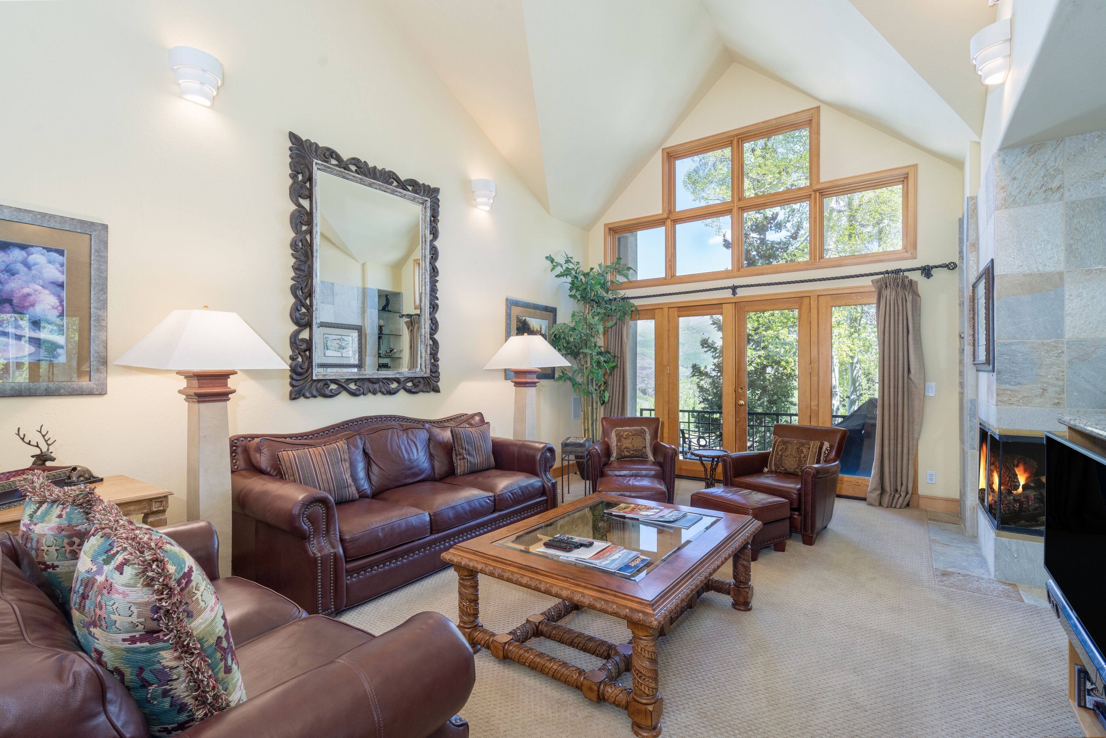 A spacious living room with a high ceiling, large windows, a fireplace, and leather furniture.