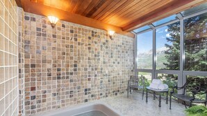 Un espace de bien-être doté d’un mur orné de mosaïques, d’un bain à remous et offrant une vue sur un paysage montagneux.