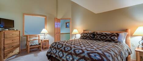 A bedroom with a bed, wooden dresser, two nightstands with lamps, a television, and a mirror.