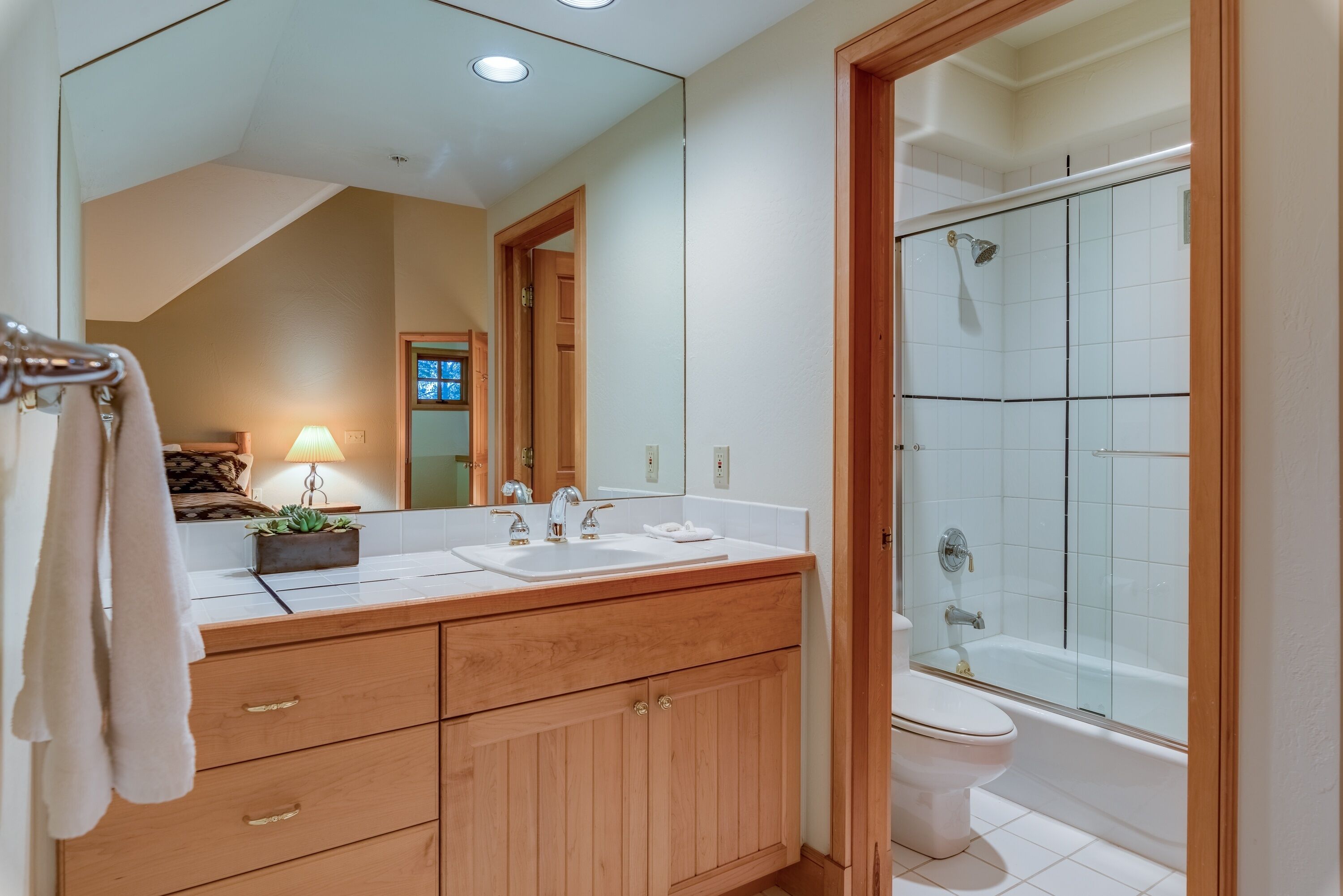 A bathroom with a wooden vanity, two sinks, a toilet, and a glass-enclosed shower.
