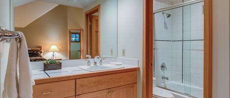 A bathroom with a wooden vanity, two sinks, a toilet, and a glass-enclosed shower.