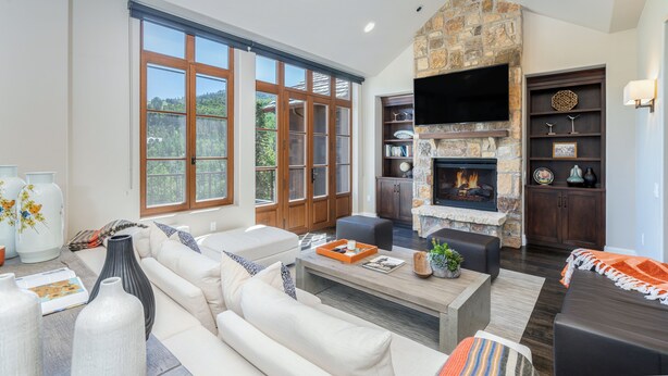 A spacious living room with a stone fireplace, large windows, and a flat-screen TV. - Slopeside Sanctuary Penthouse 3 Bedroom Condo by Alpine Lodging Telluride (Telluride)