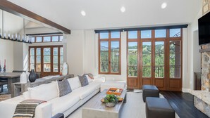 A spacious living room with a large window, a stone fireplace, and a modern kitchen area. - Slopeside Sanctuary Penthouse 3 Bedroom Condo by Alpine Lodging Telluride (Telluride)