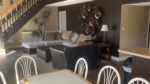 En rummelig opholdsstue med trappe, hjørnesofa, spisebord med stole og en dekorativ vægdekoration.
