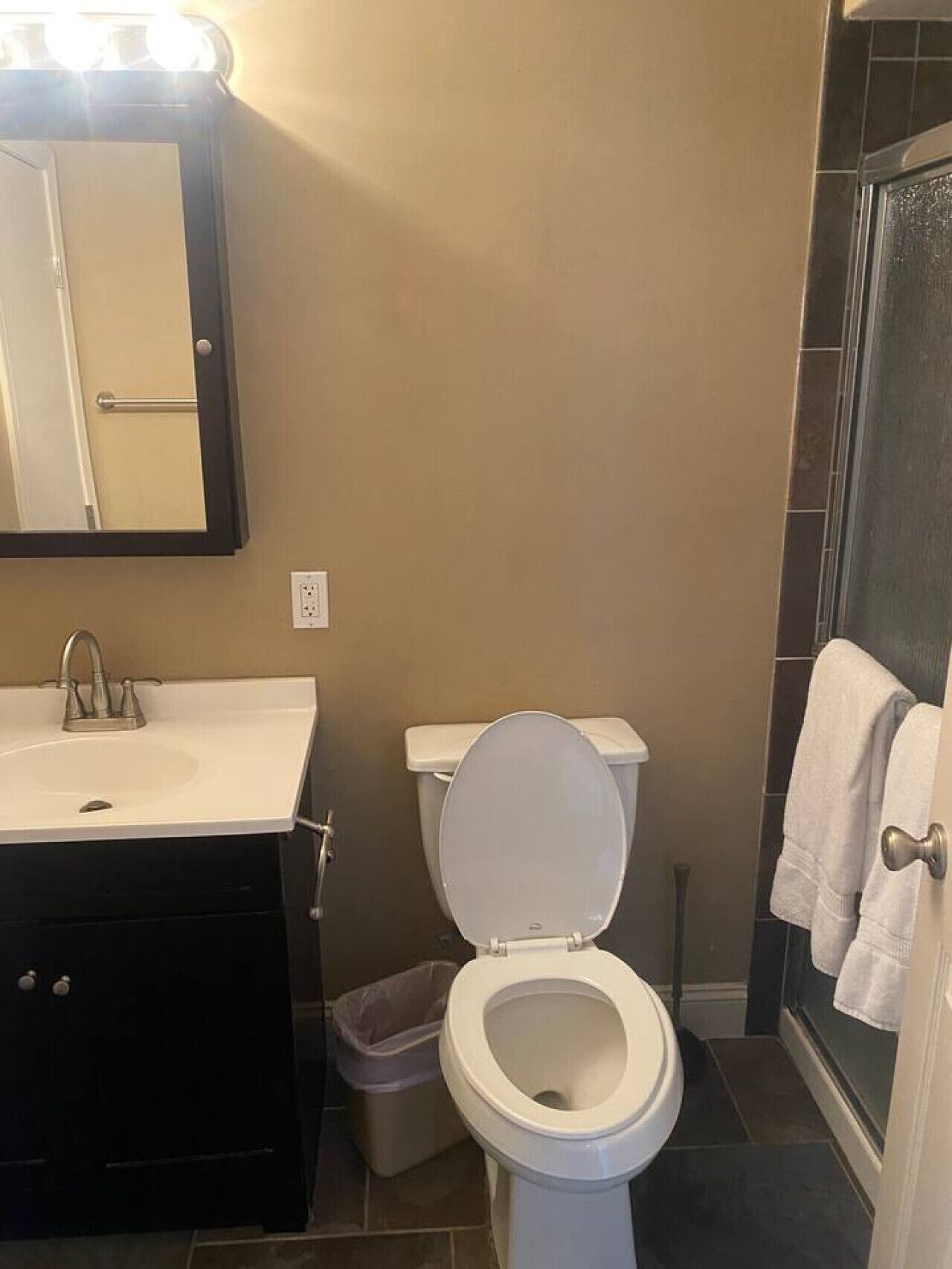 Un baño con inodoro blanco, lavamanos con espejo y zona de ducha.