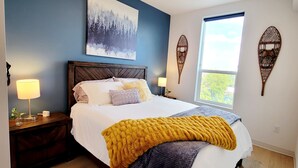 A bedroom with a bed, two bedside tables, a window, and a wall-mounted artwork. - Bozeman Summer Getaway: Climate-Controlled Garage + Mountain Views! (Bozeman)