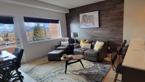 A modern living room with a sofa, a coffee table, and a view of mountains through large windows. - Bozeman Summer Getaway: Climate-Controlled Garage + Mountain Views! (Bozeman)