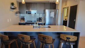 A modern kitchen with a central island, bar stools, a microwave, and a refrigerator. - Bozeman Summer Getaway: Climate-Controlled Garage + Mountain Views! (Bozeman)