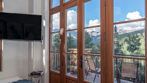 A bedroom with a large window, a bed, a TV, and a small table with a book. - Mt Wilson Basecamp 4 Bedroom Condo by Alpine Lodging Telluride (Telluride)