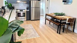 A modern kitchen with grey cabinets, stainless steel appliances, a wooden dining table, and a large green plant. - Serenity by the Sea (Samoa)